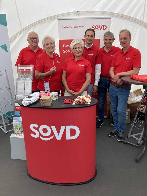 Sechs Personen in einem Infozelt an einem Pult mit dem SoVD-Logo. 