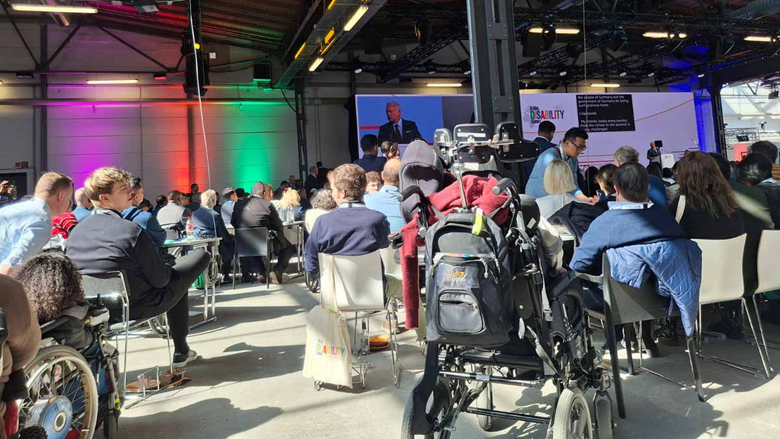 Voll besetzter Veranstaltungssaal; viele Besucher im Rollstuhl. 