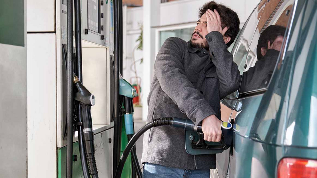 Ein Mann tankt sein Auto und blickt besorgt auf die Preisanzeige. 
