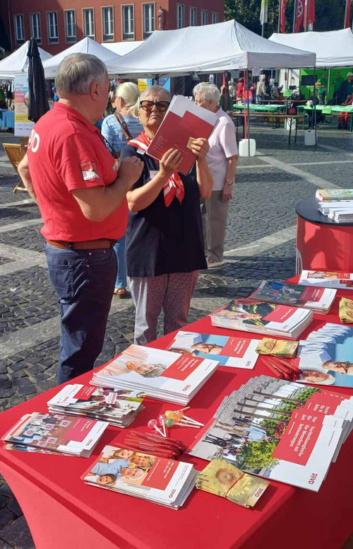 Mann und Frau am Gespräch an einem Stand mit vielen Flyern und Broschüren. 