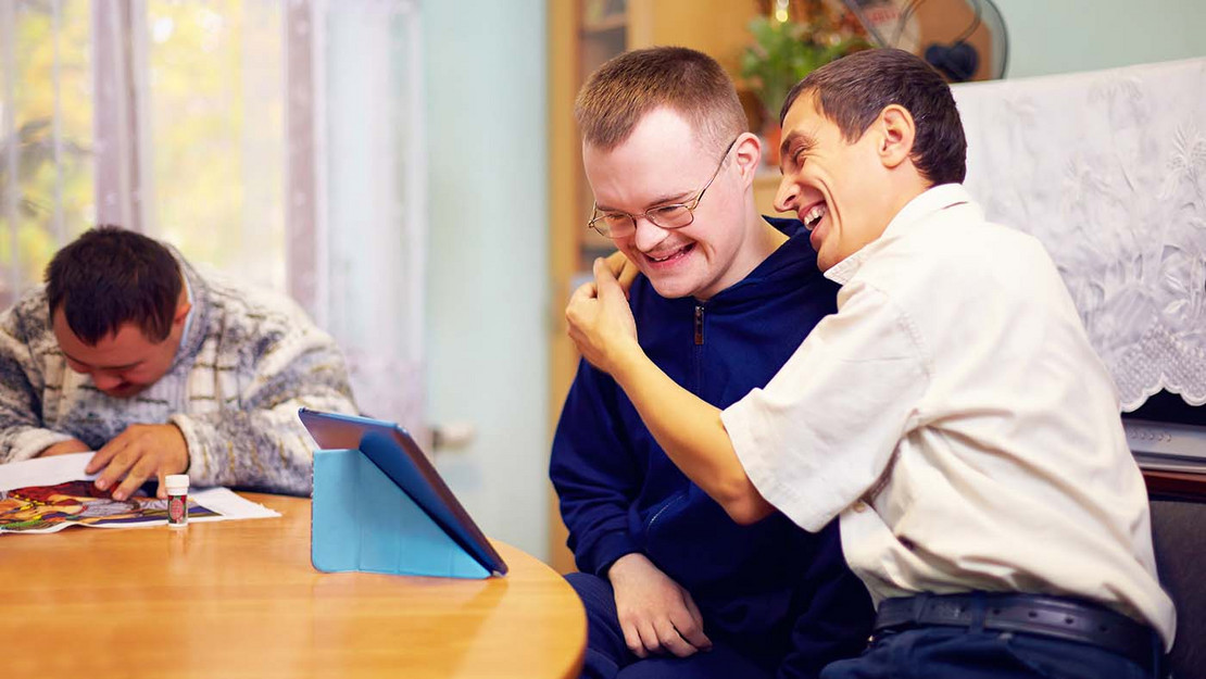 Menschen mit Behinderung schauen gemeinsam auf ein Tablet. 
