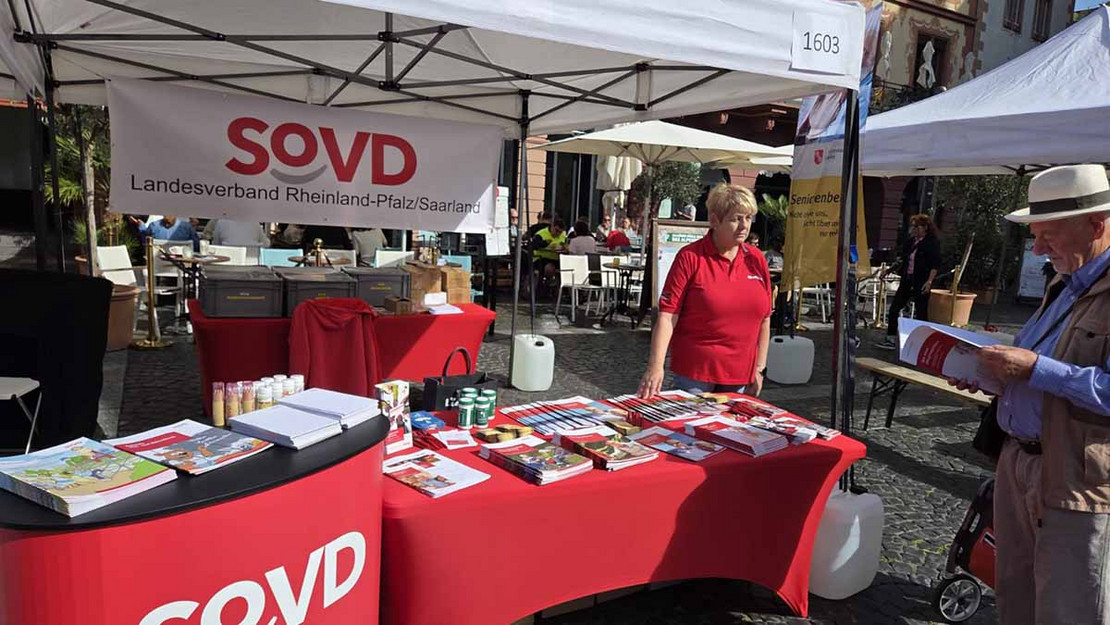 Eine Frau steht am einem Infostand des SoVD und spricht mit einem Besucher. 