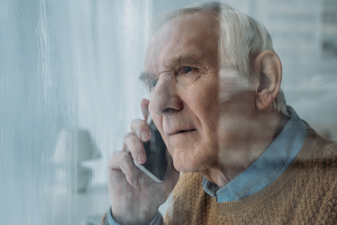 Älterer Mann telefoniert hinter einer Scheibe. 