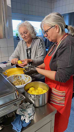 Zwei Frauen am Herd schälen Kartoffeln.