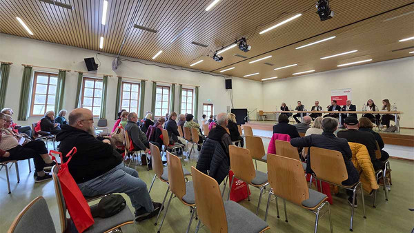 Foto eines Veranstaltungssaals mit vielen besetzten Stühlen. 