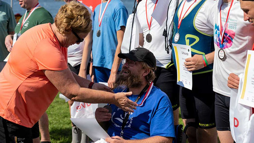 Michaela Engelmeier überreicht einem Rollstuhlfahrer eine Medaille. 