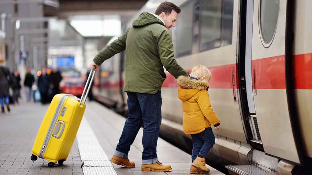Vater und Sohn mit Koffer steigen am Bahnhof in einen ICE. 