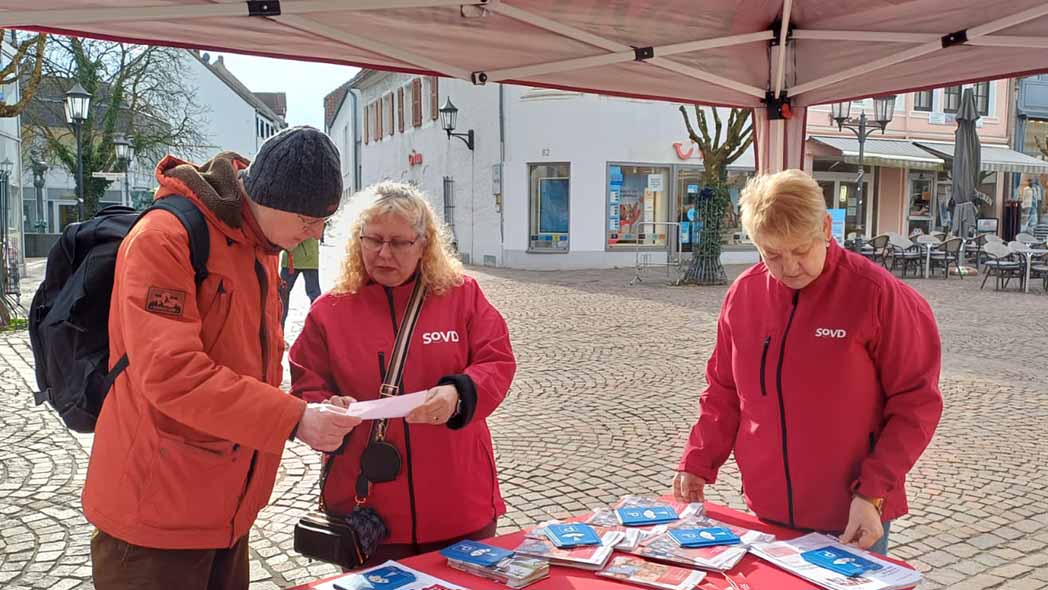 Zwei SoVD-Frauen im Gespräch mit einem Besucher am Stand.