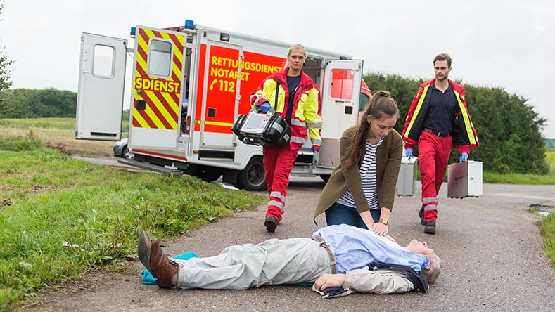 podiumsdiskussion_kusel_benjaminnolte_AdobeStock Mann liegt auf Straße, eine Frau animiert ihn, zwei Rettungssanitäter kommen auf sie zu